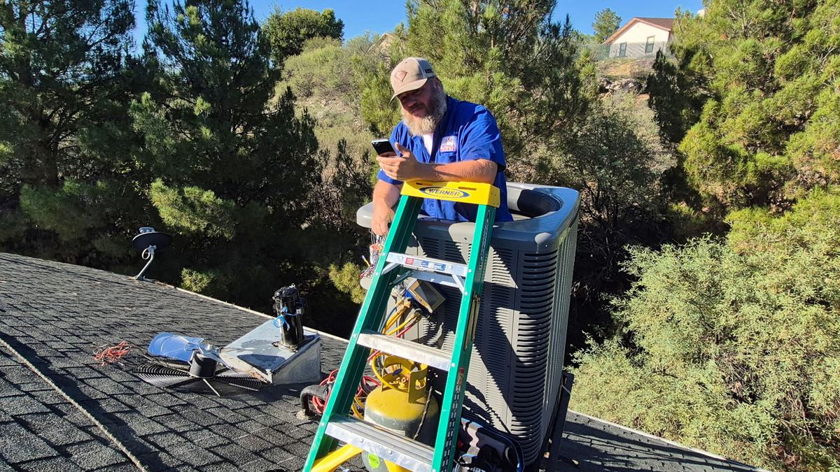 Nichols technician on a ladder servicing a rooftop AC unit in Prescott